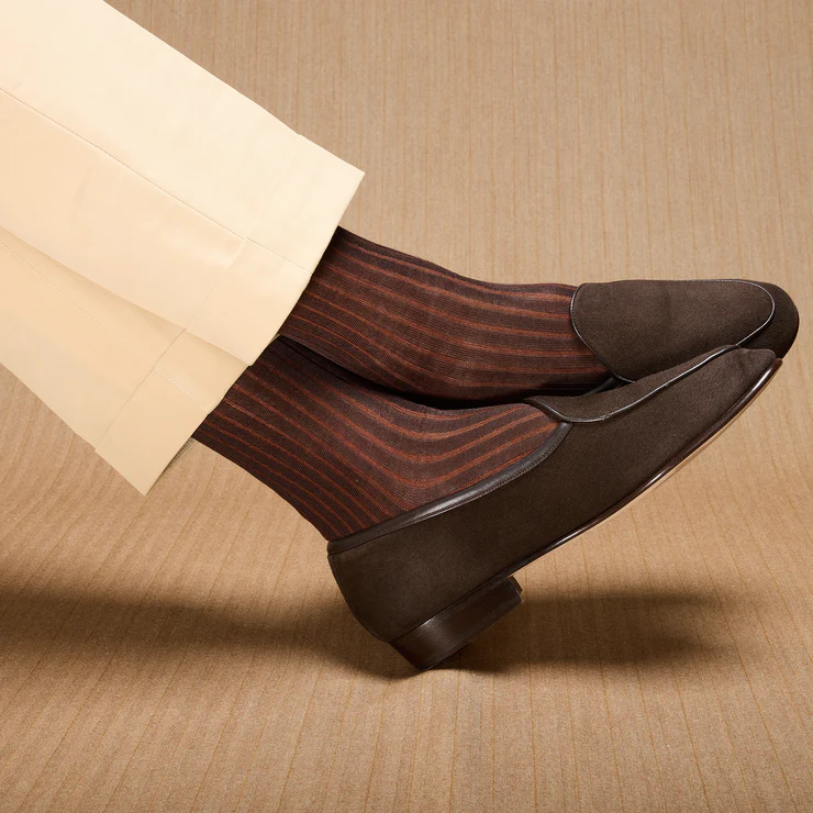 A pair of brown loafers worn with brown and rust striped socks, partially visible beneath cream-colored trousers.