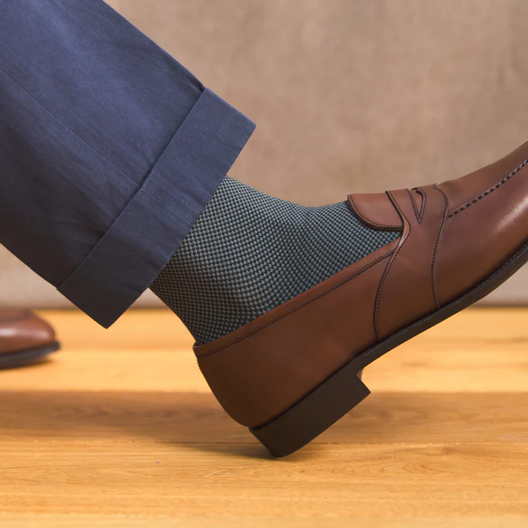 A brown leather shoe is paired with a dark blue patterned sock, partially visible below navy trousers.