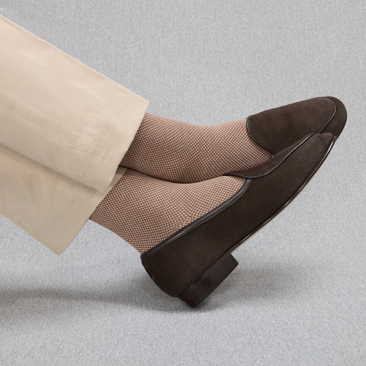 A pair of brown suede loafers worn with light brown patterned socks.