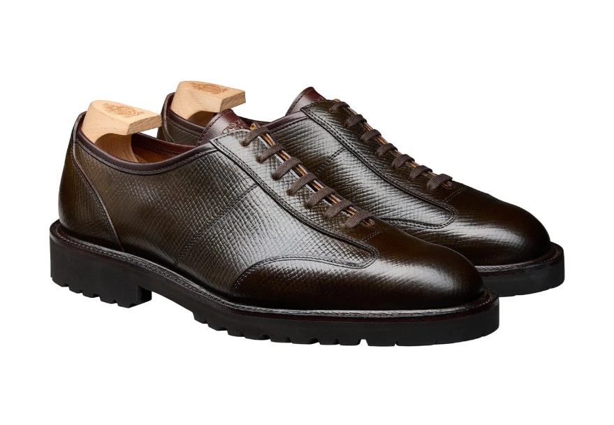 A pair of dark brown leather shoes with a textured finish and wooden shoe trees inserted.