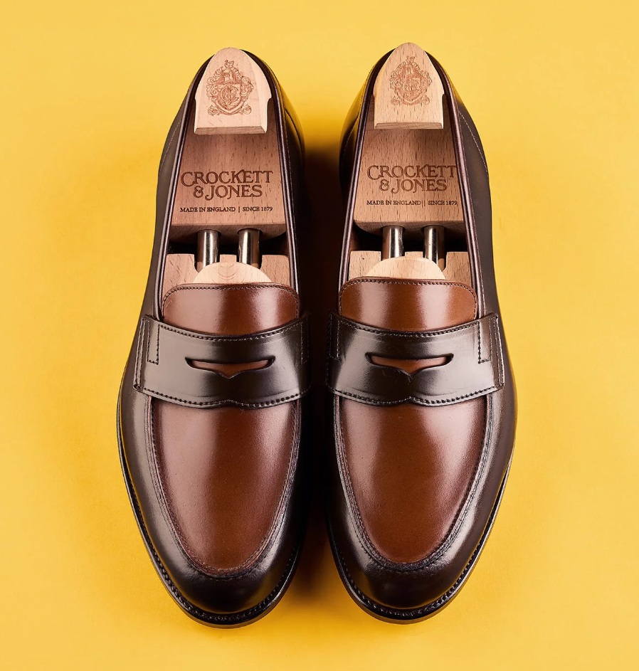 A pair of dark brown and tan leather loafers with wooden shoe trees inside.