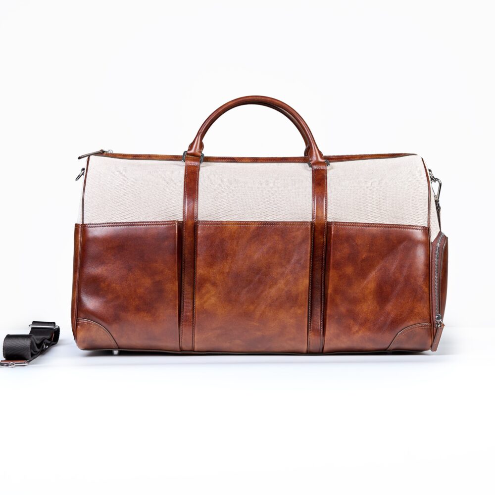 A brown leather duffel bag with a beige canvas top and two handles.