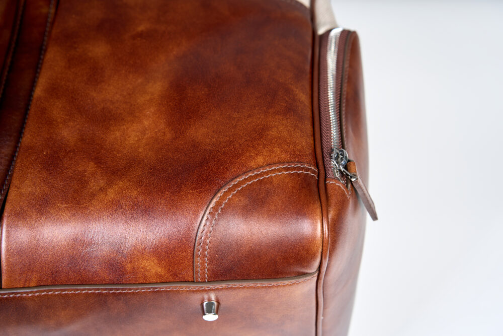 A close-up of a brown leather bag featuring a silver zipper and stitched details.