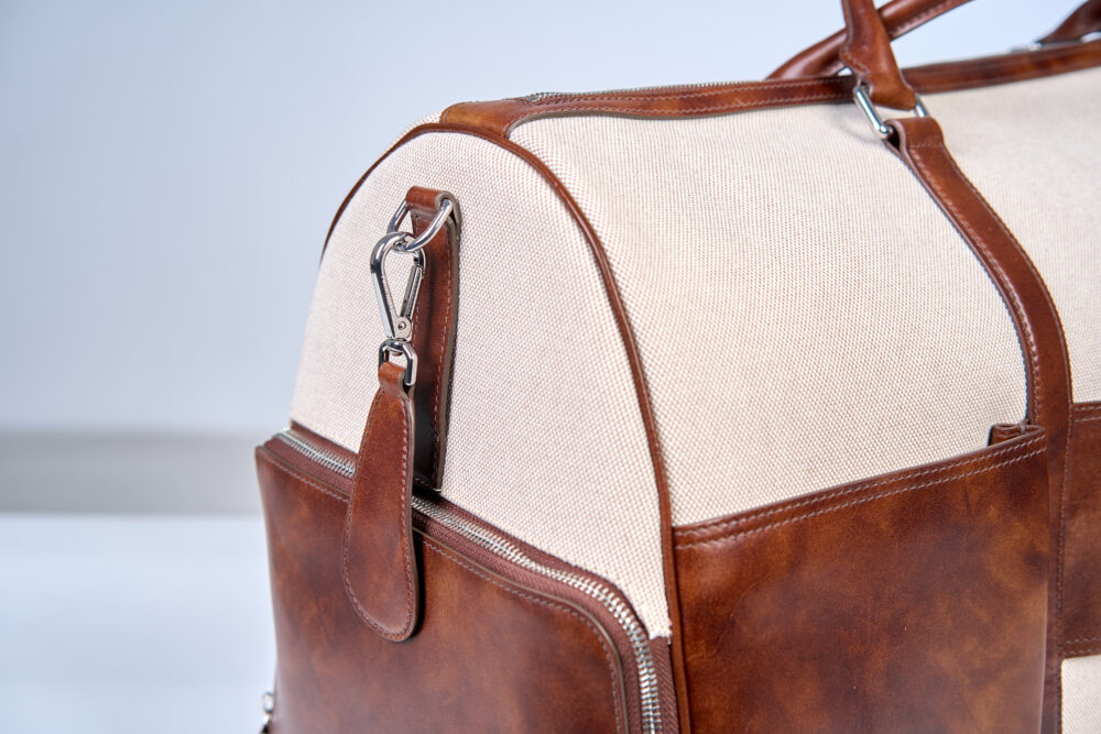 A beige canvas bag with brown leather accents and a silver zipper.