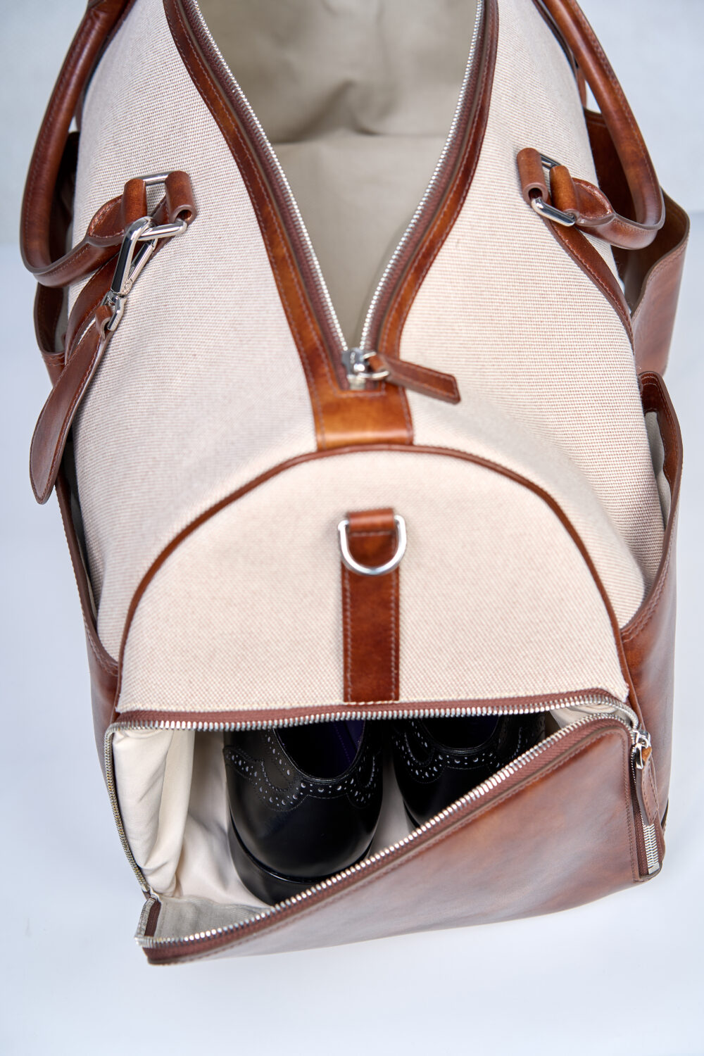 A tan and brown duffel bag partially unzipped, revealing a pair of black shoes inside.