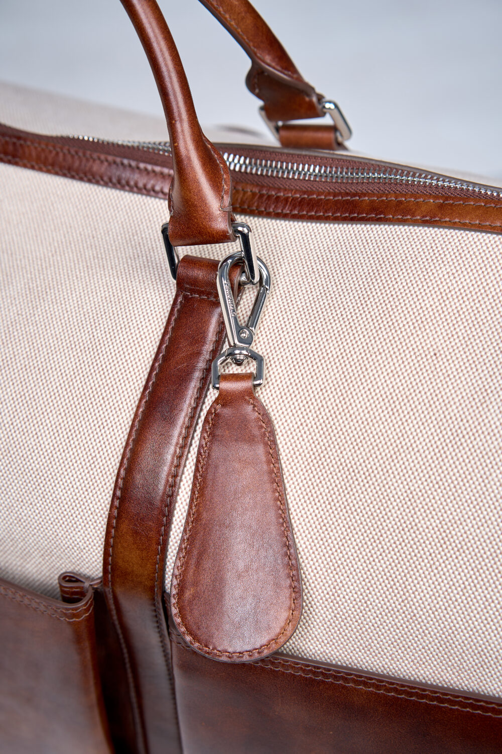 A close-up of a brown leather strap attached to a beige canvas bag.