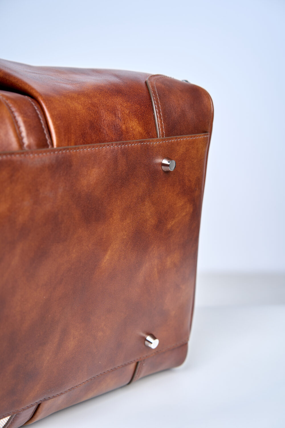 A close-up of a brown leather bag featuring silver metal studs on the bottom.