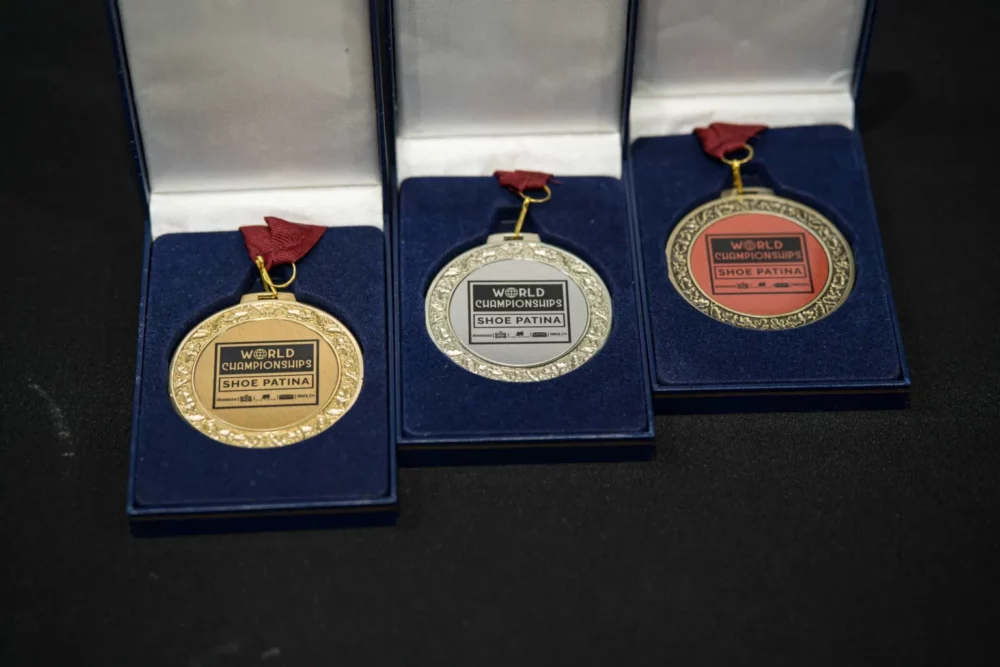 Three medals for "World Championships Shoe Patina" in gold, silver, and bronze, displayed in blue velvet boxes.