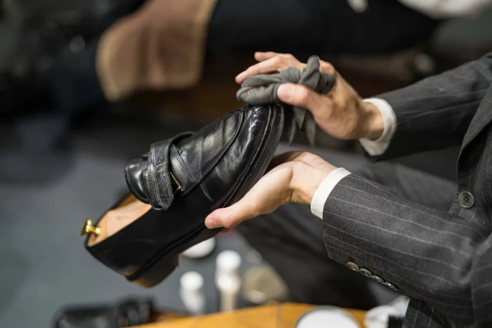 A person in a suit is polishing a black leather shoe with a cloth.