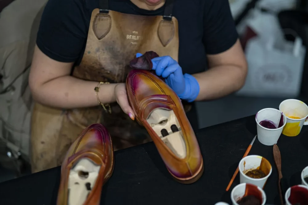 A person wearing blue gloves is polishing a pair of brown leather shoes with a gradient finish.
