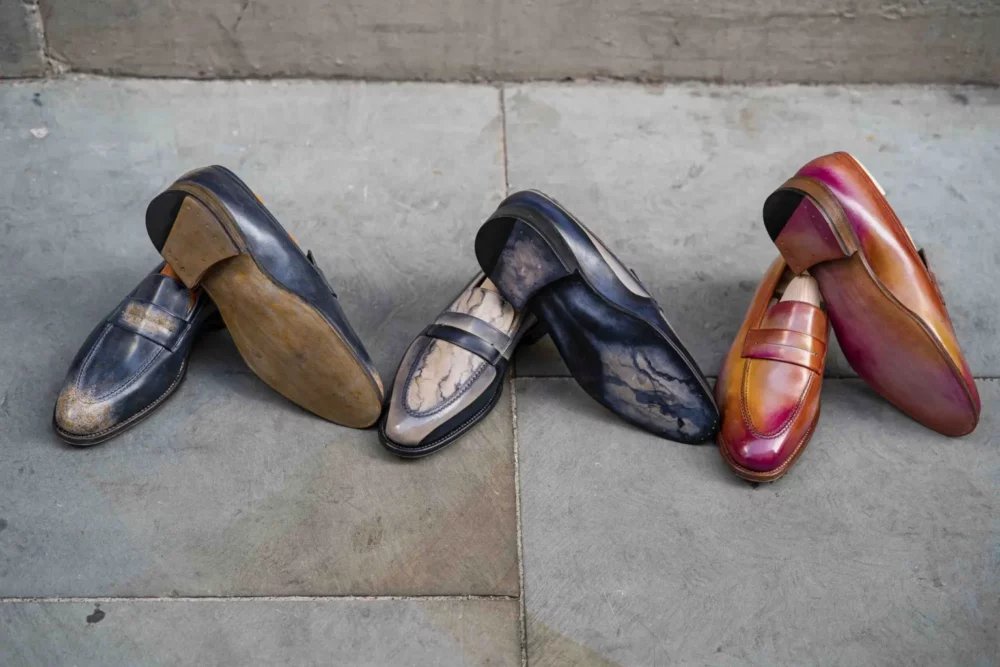 Three pairs of leather shoes in varying colors: dark blue, light gray with marbling, and reddish-brown.