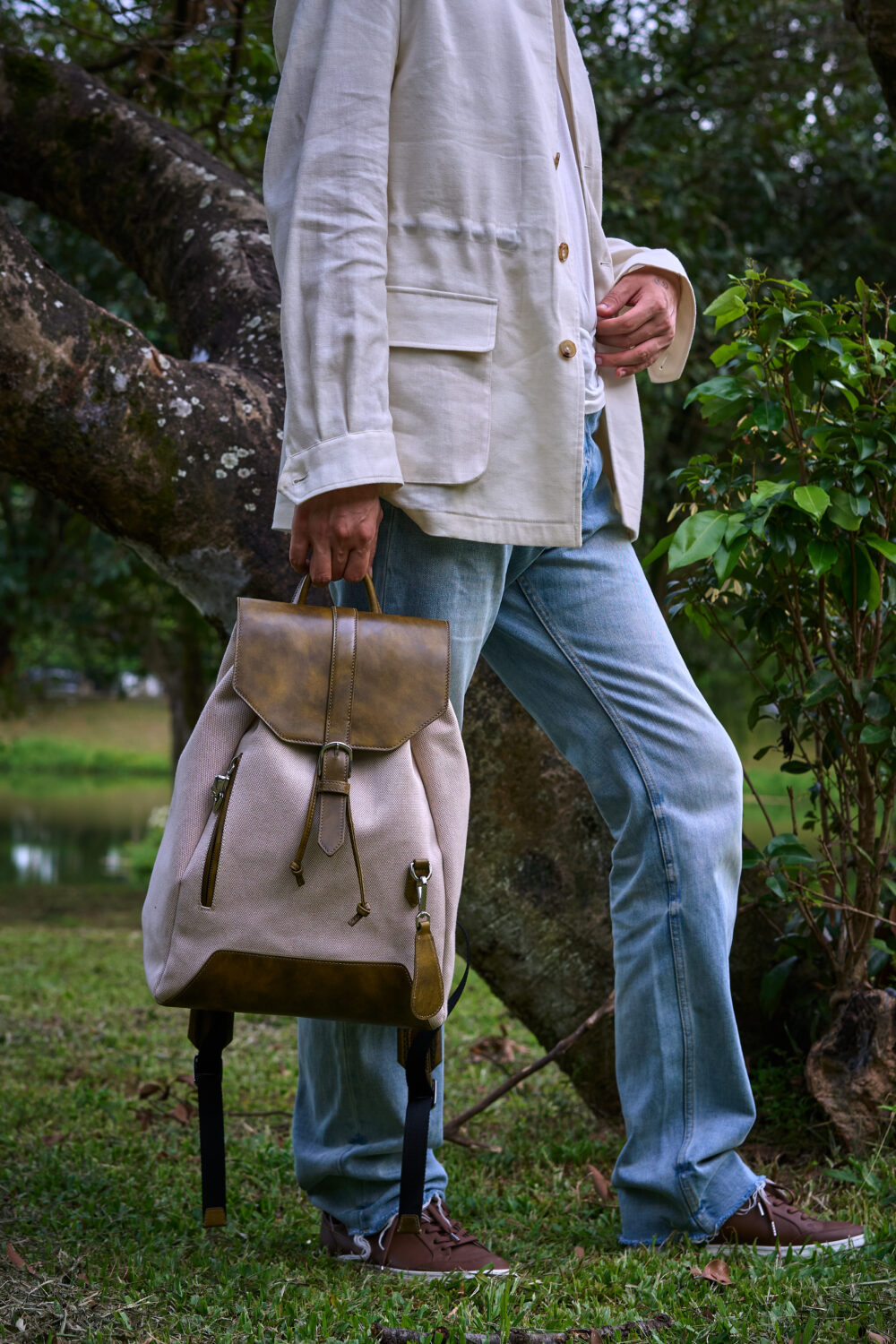 A person in a light-colored jacket holds a beige and brown backpack.