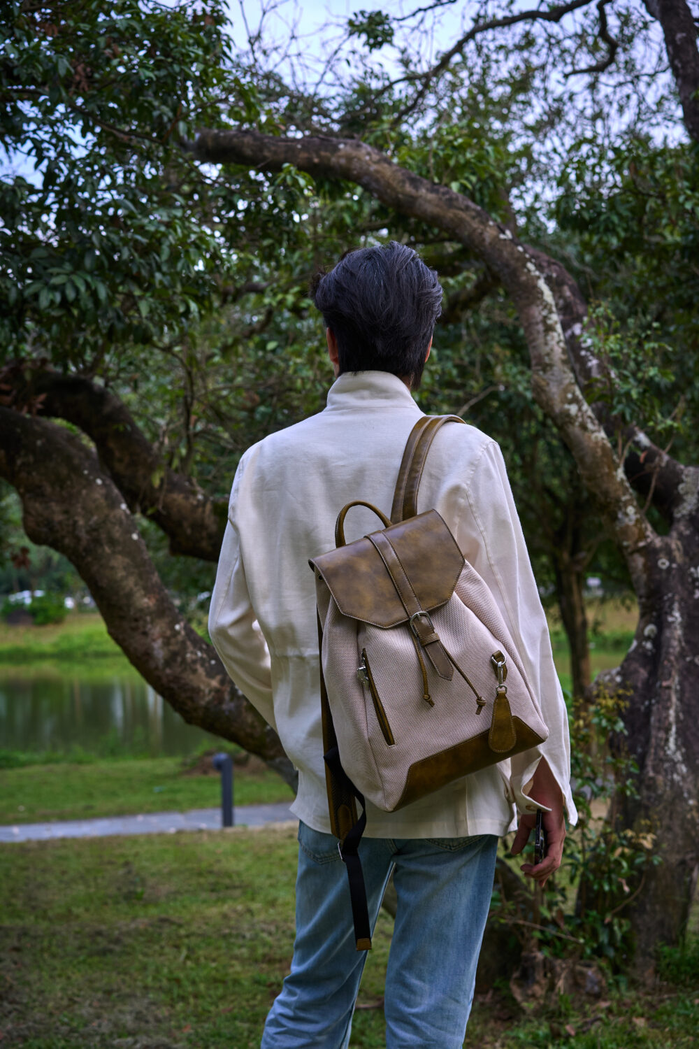 A person wearing a light-colored shirt and blue jeans carries a beige and brown backpack.