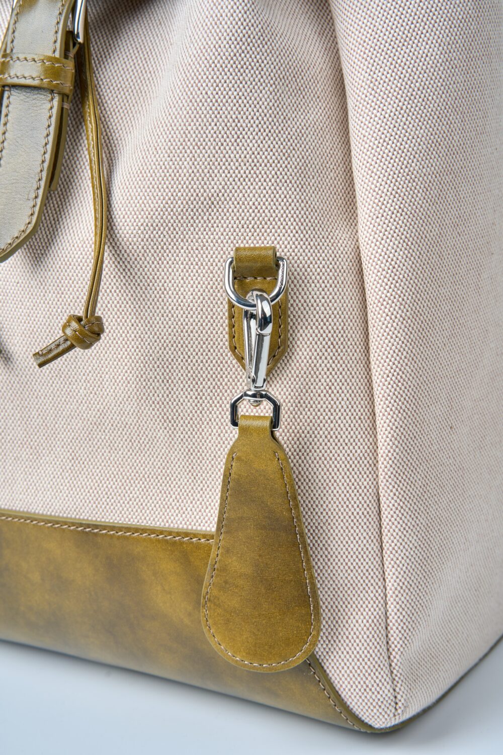 A close-up of a beige bag with a brown leather base and a silver clasp.