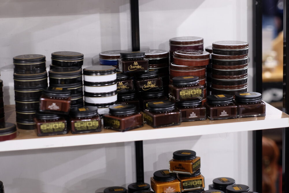A variety of Saphir shoe care products from the MDO line in small jars and tins, featuring black, white, and brown colors,