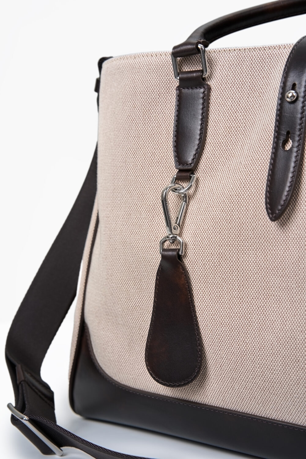 A beige canvas bag with dark brown leather accents and a silver clip.