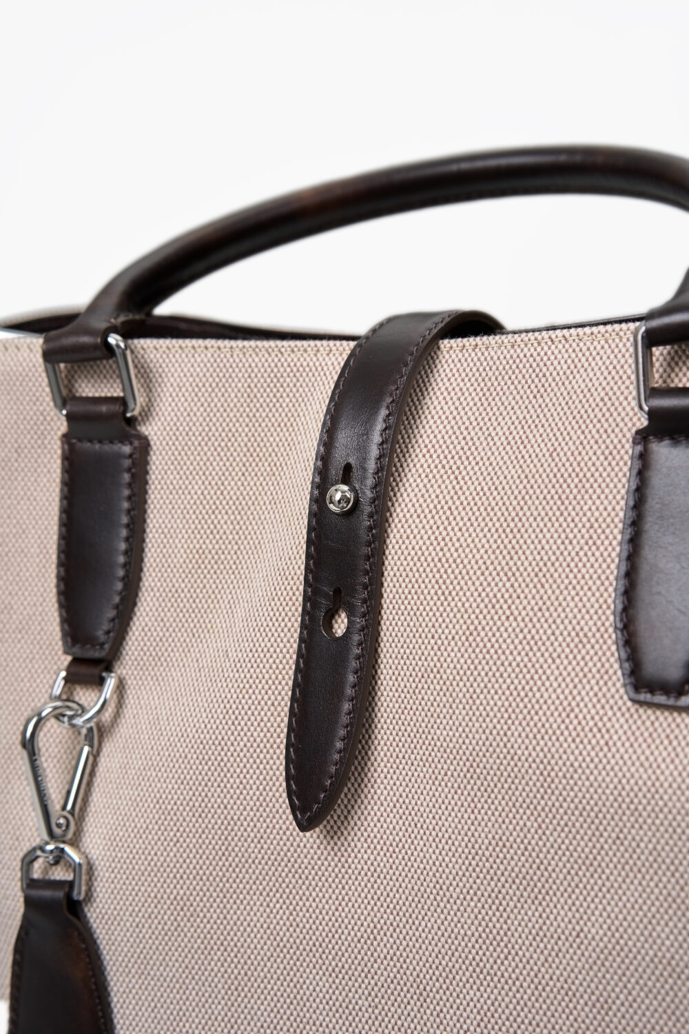 A close-up of a beige fabric bag with dark brown leather straps and a silver clasp.