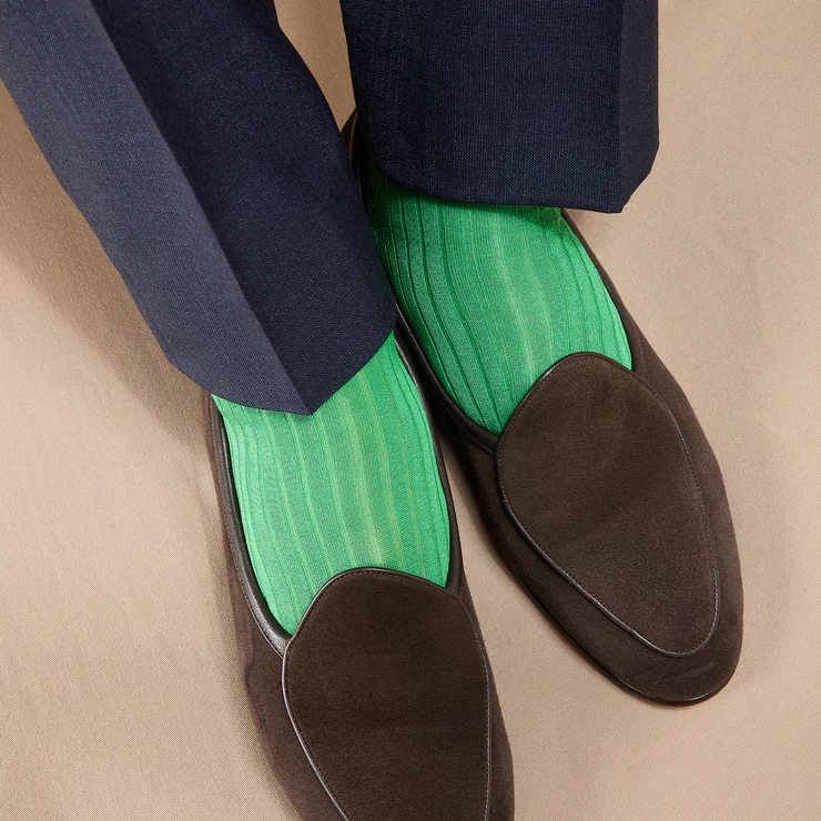 A pair of feet wearing dark brown loafers and bright green striped socks, with navy trousers visible above.