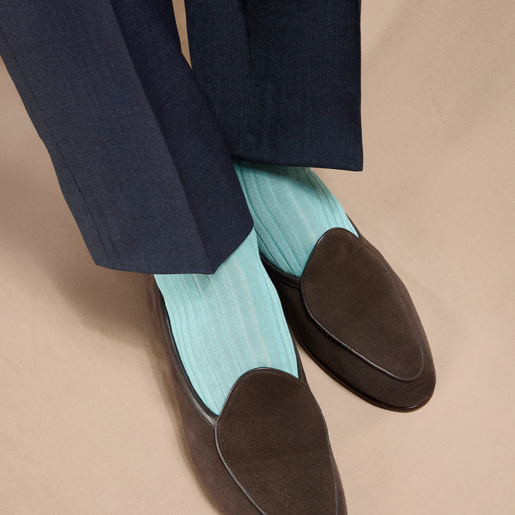 A pair of brown loafers paired with light blue striped socks, worn with dark blue trousers.