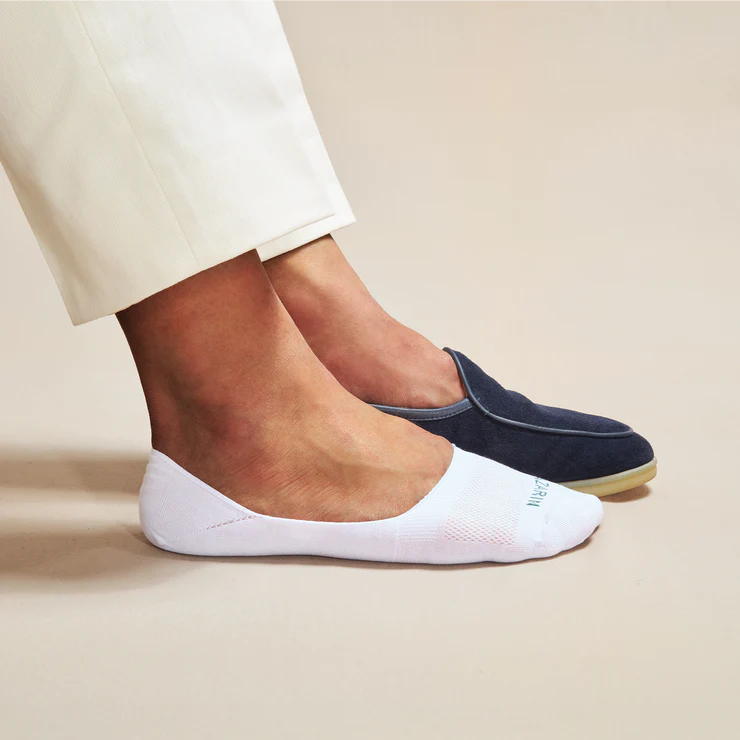 A foot wearing a white sock is paired with a foot in a dark blue slip-on shoe.