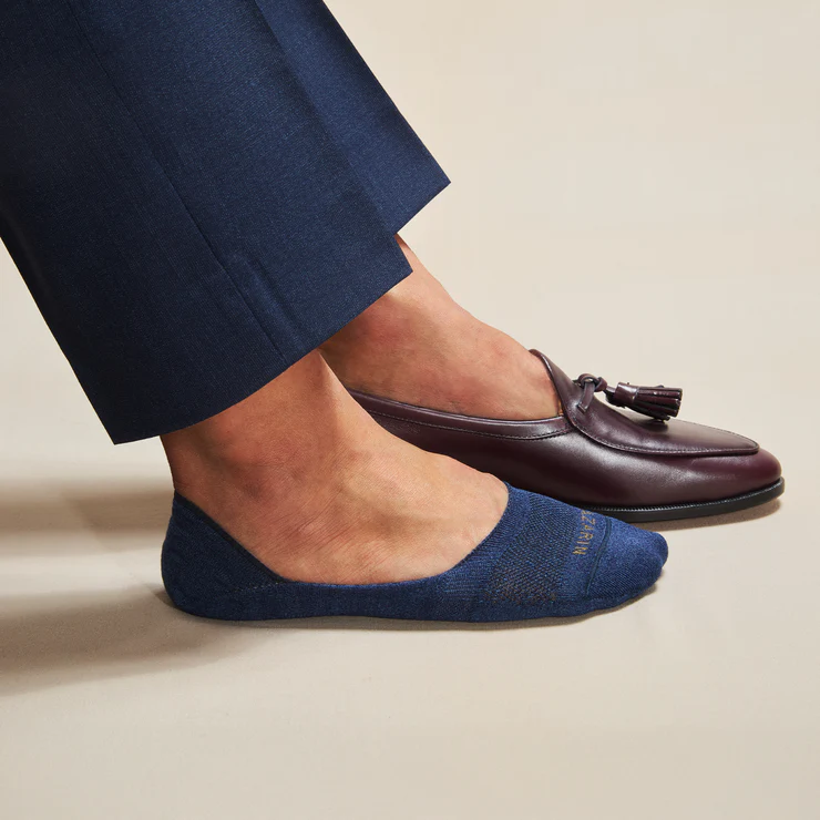 A foot wearing a dark blue sock is next to a foot in a burgundy leather loafer.