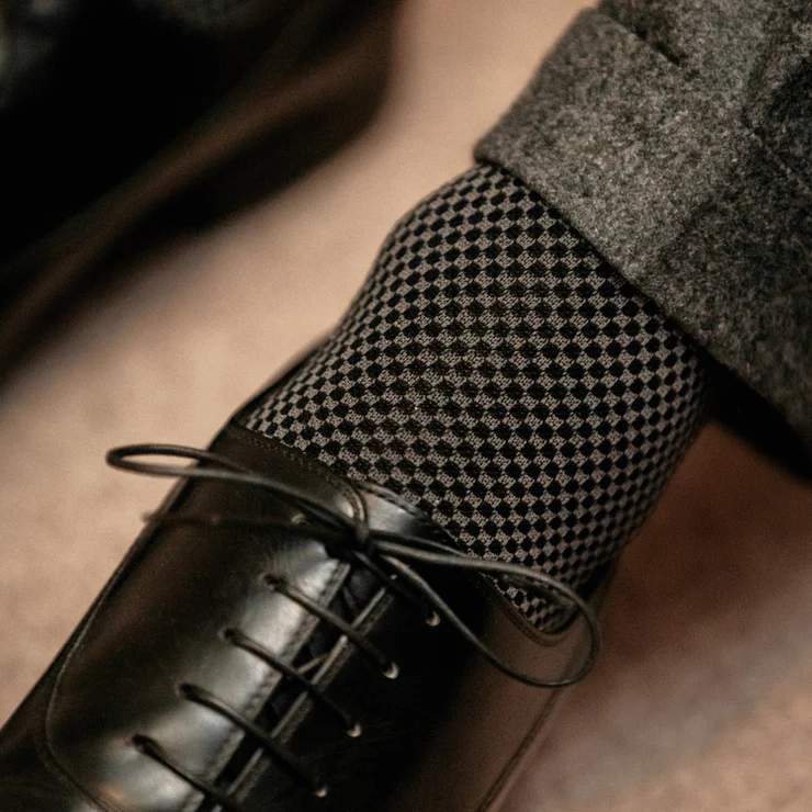 A close-up of a black dress shoe paired with a dark checkered sock.