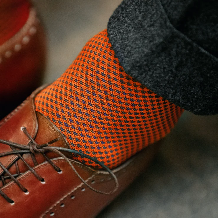 A close-up of a brown leather shoe paired with an orange and navy patterned sock.
