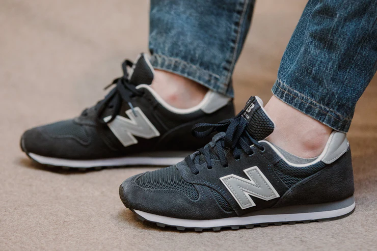 A person is wearing dark gray New Balance sneakers with a light gray logo.