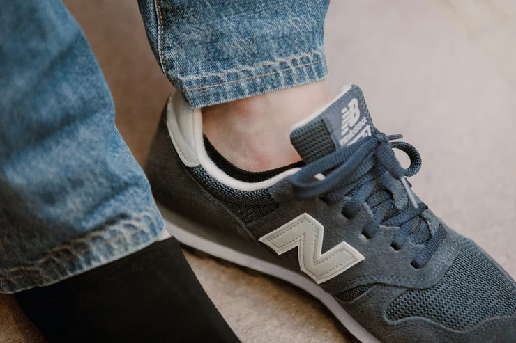 A close-up of a foot wearing a gray New Balance sneaker next to a bare foot.