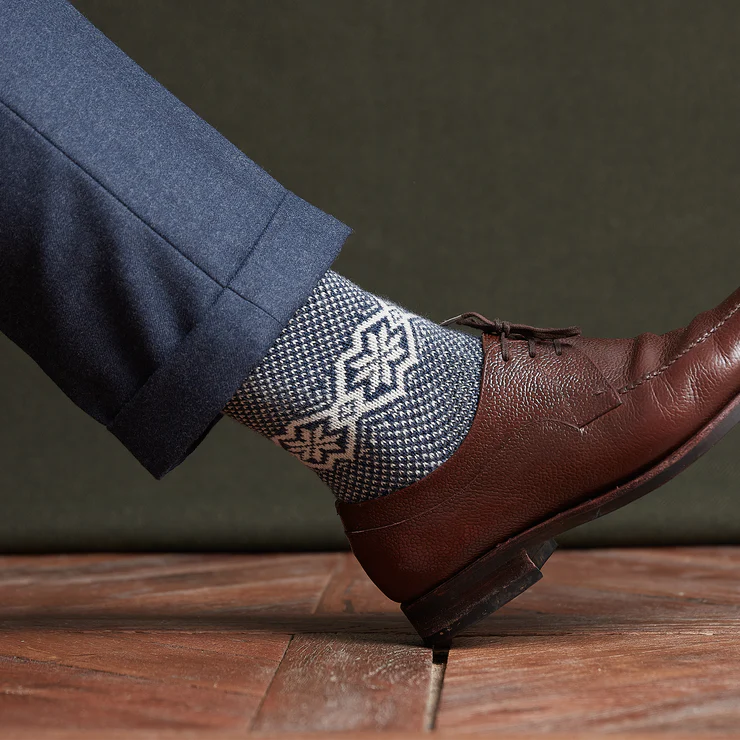 A brown leather shoe is paired with patterned blue and white socks, worn with navy trousers.