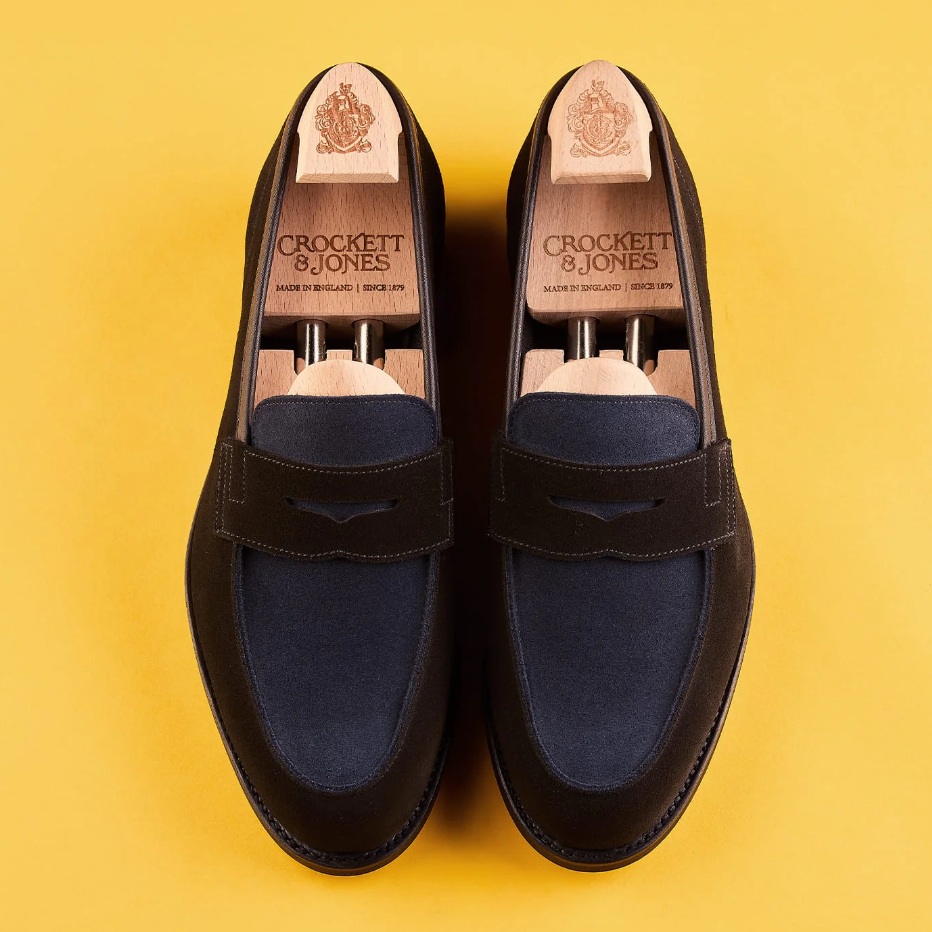 A pair of elegant dark brown and navy loafers with wooden shoe trees inside.