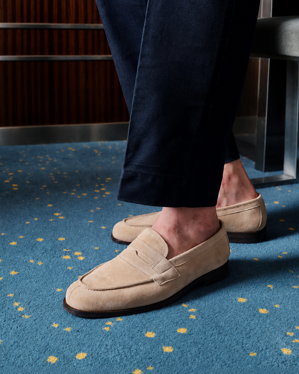Beige suede loafers worn with dark trousers.