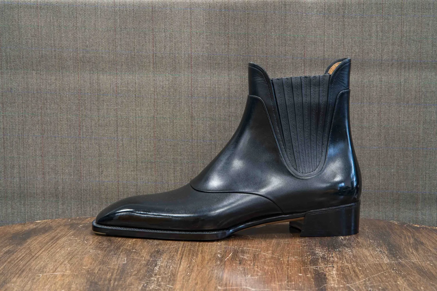 A sleek black leather ankle boot with a textured elastic panel.