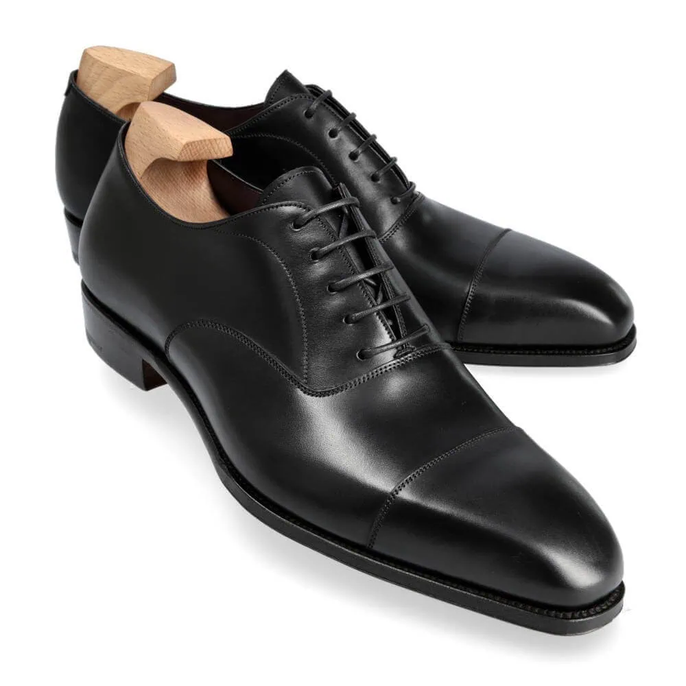 A pair of black leather dress shoes with wooden shoe trees inserted.