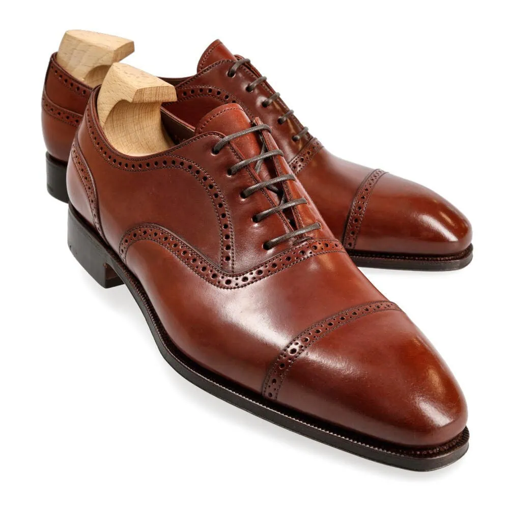 Brown leather dress shoes with decorative perforations and wooden shoe trees inside.