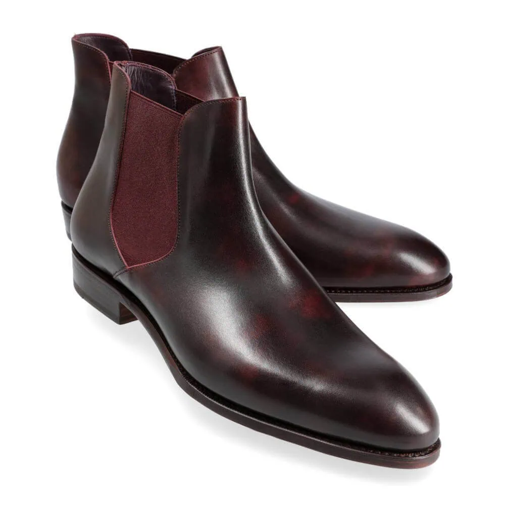 A pair of dark burgundy leather chelsea boots with elastic side panels.