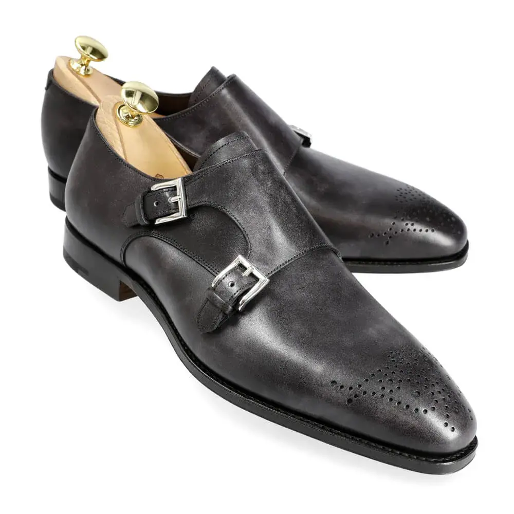 A pair of black leather double monk strap shoes with silver buckles and decorative perforations.