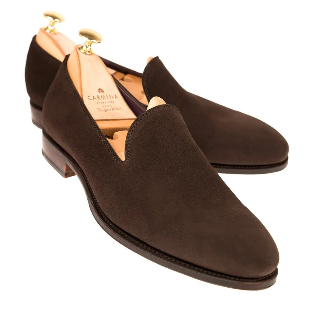 A pair of dark brown suede slip-on shoes with a sleek design and wooden shoe trees inside.