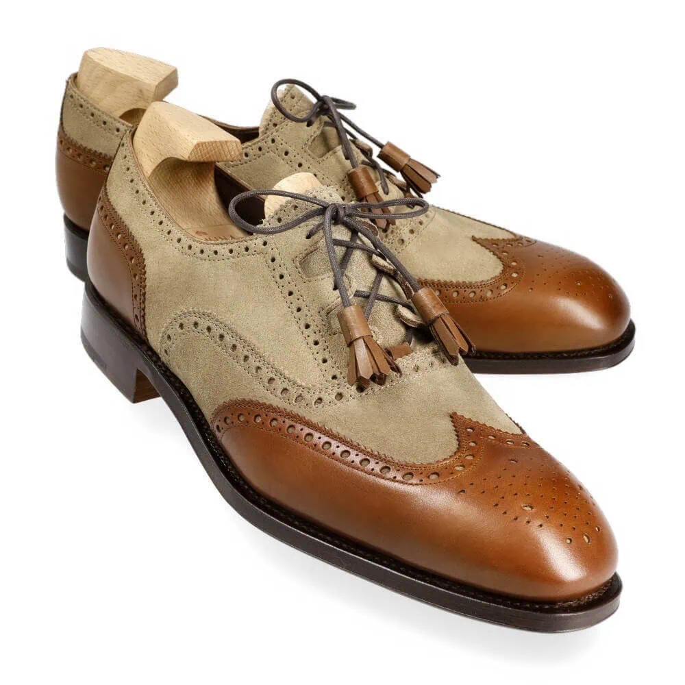 A pair of men's dress shoes featuring a light beige suede upper and brown leather accents with decorative perforations.