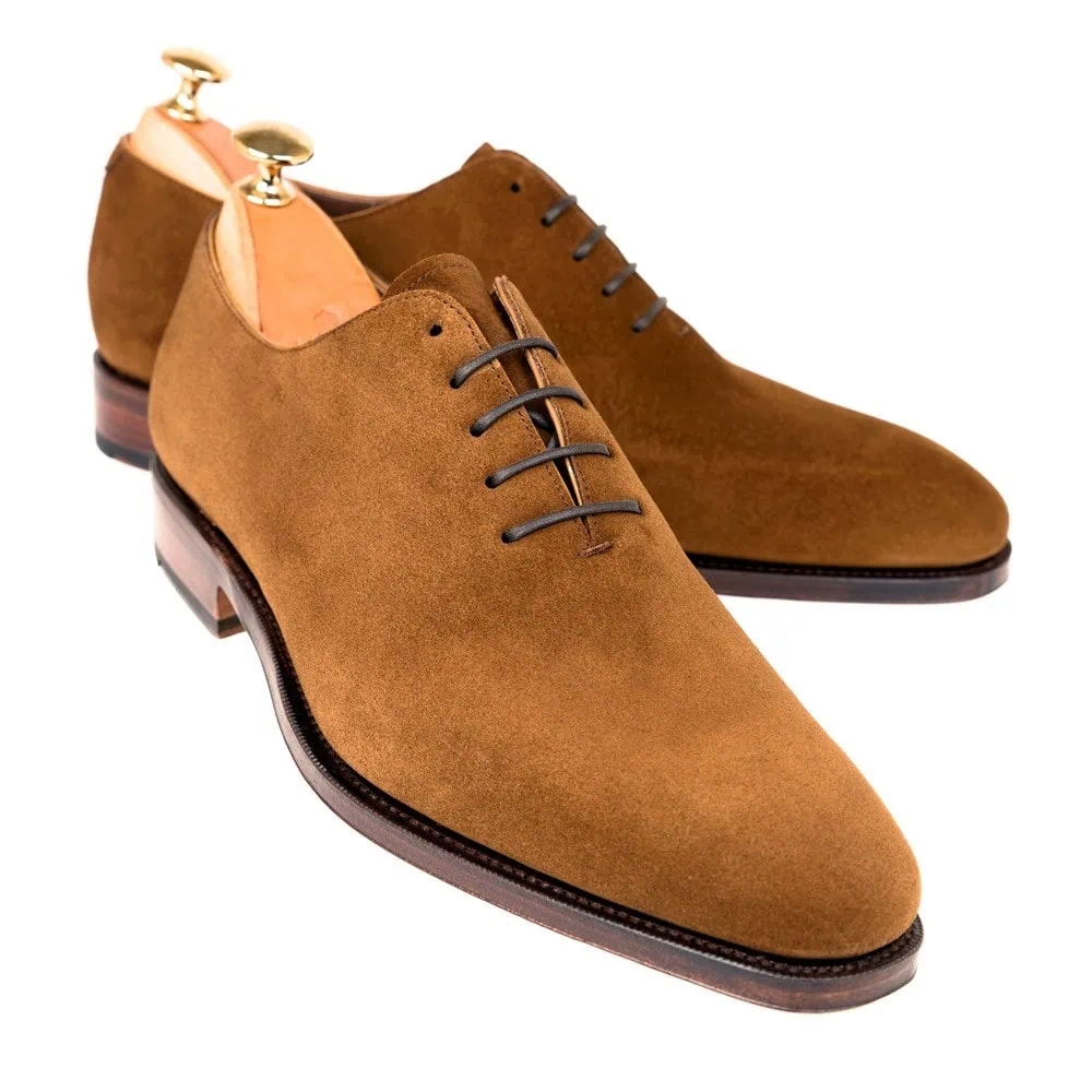 A pair of brown suede dress shoes with laces and wooden shoe trees.