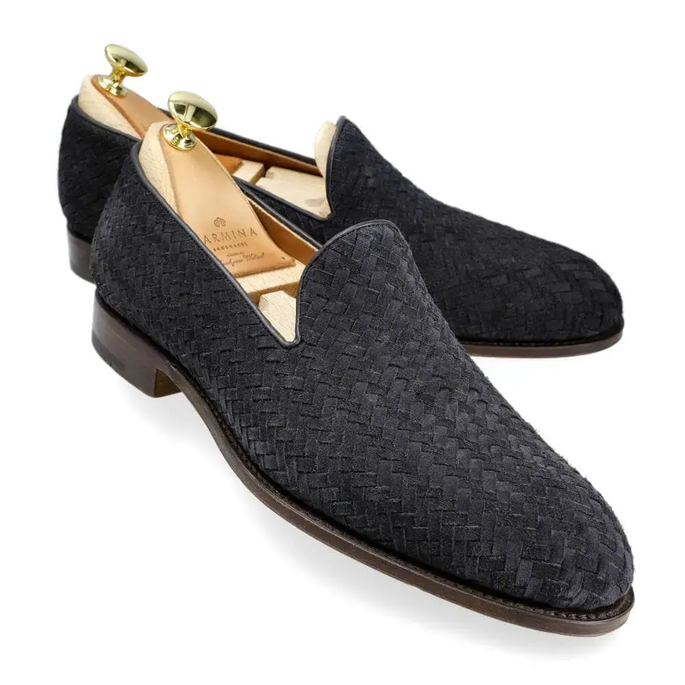 A pair of black woven loafers with a smooth leather sole and gold shoehorns inside.