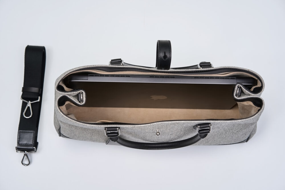 A gray laptop bag with a black strap, showing a laptop inside.