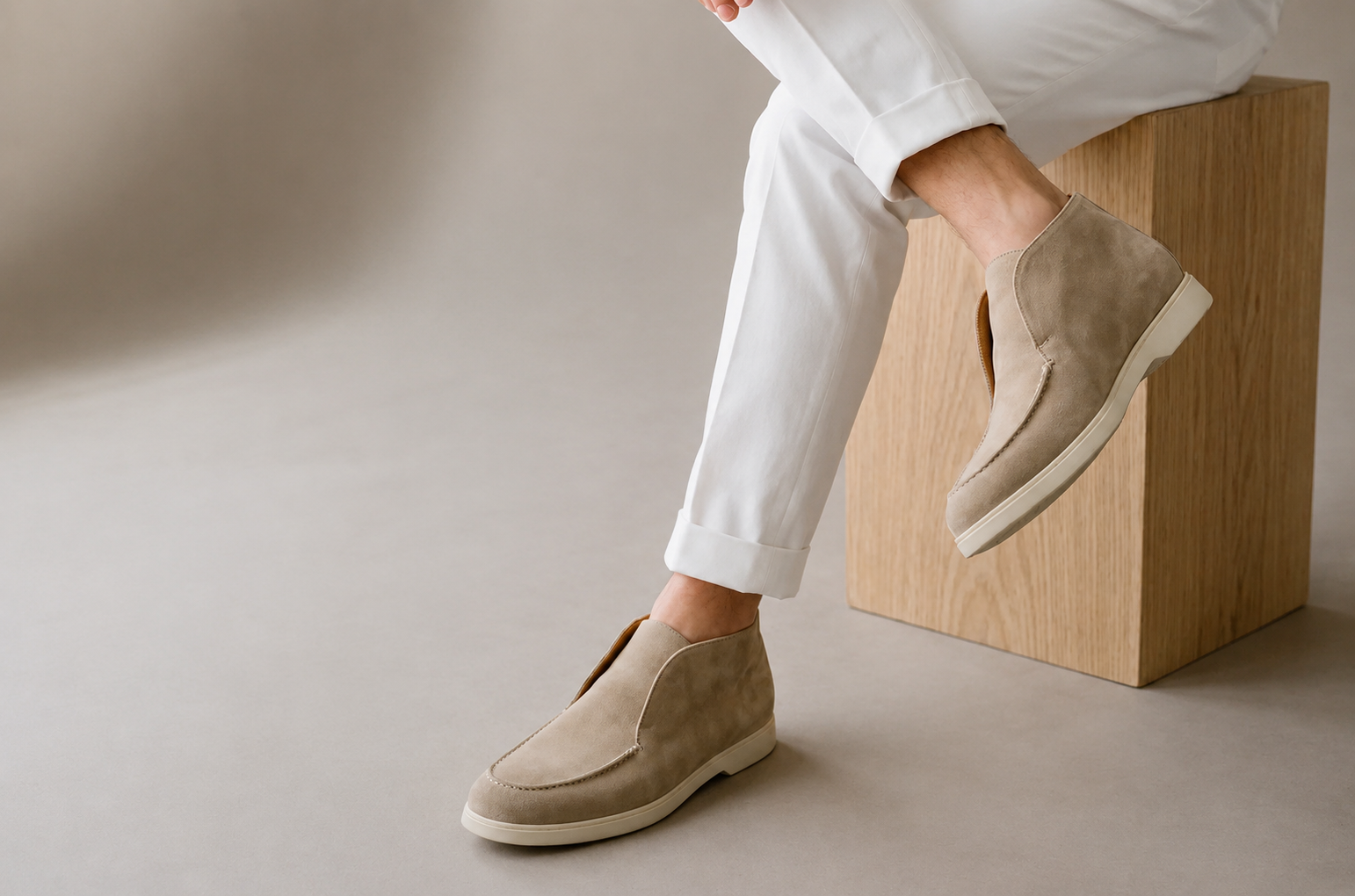 A close-up of a foot wearing a light brown suede TLB Mallorca Laceless Ankle Boots, paired with white cuffed pants.