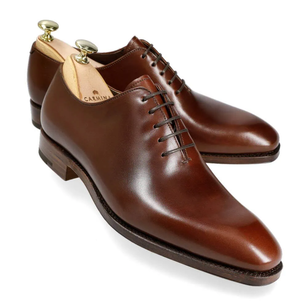 A pair of polished brown leather dress shoes with laces and shoe trees inserted.