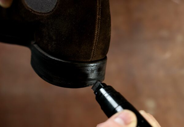 A hand holds a black marker being used to touch up the black heel of a brown suede shoe.