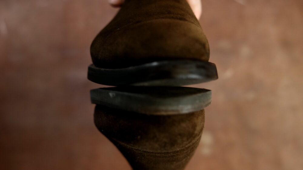 A close-up of a brown suede shoe with a black rubber sole.