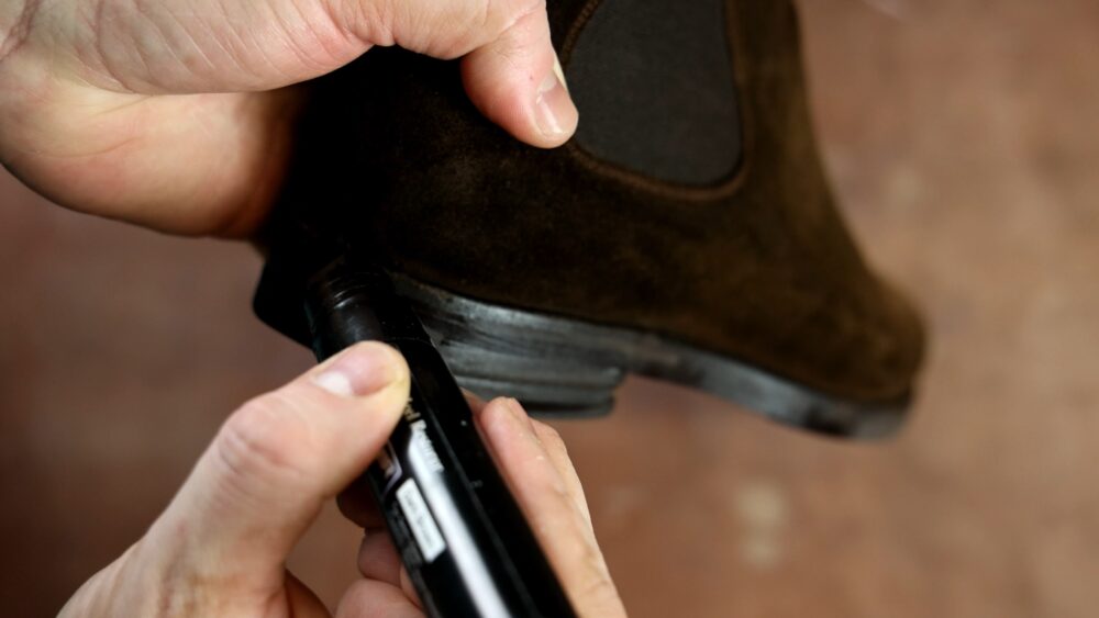 A person is applying a black marker to the heel of a brown suede boot.