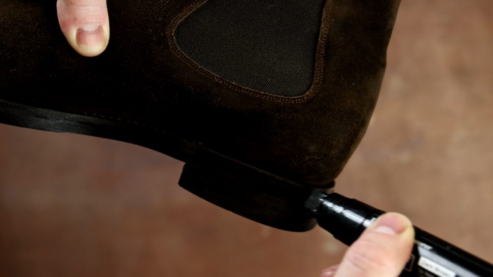 A brown suede shoe with a textured black panel is being marked with a black pen.