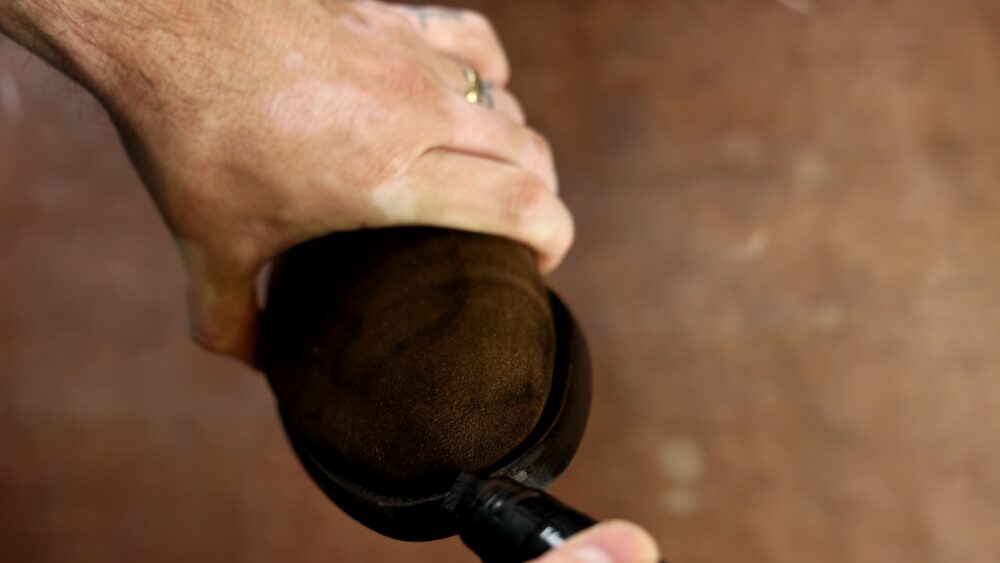 A hand holds a brown suede shoe while applying a black marker to its edge.