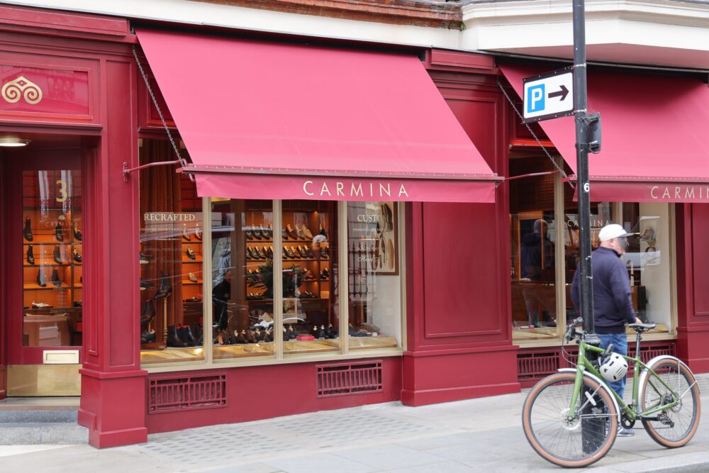A storefront with a red facade and a sign reading "CARMINA," displaying various shoes in the window.